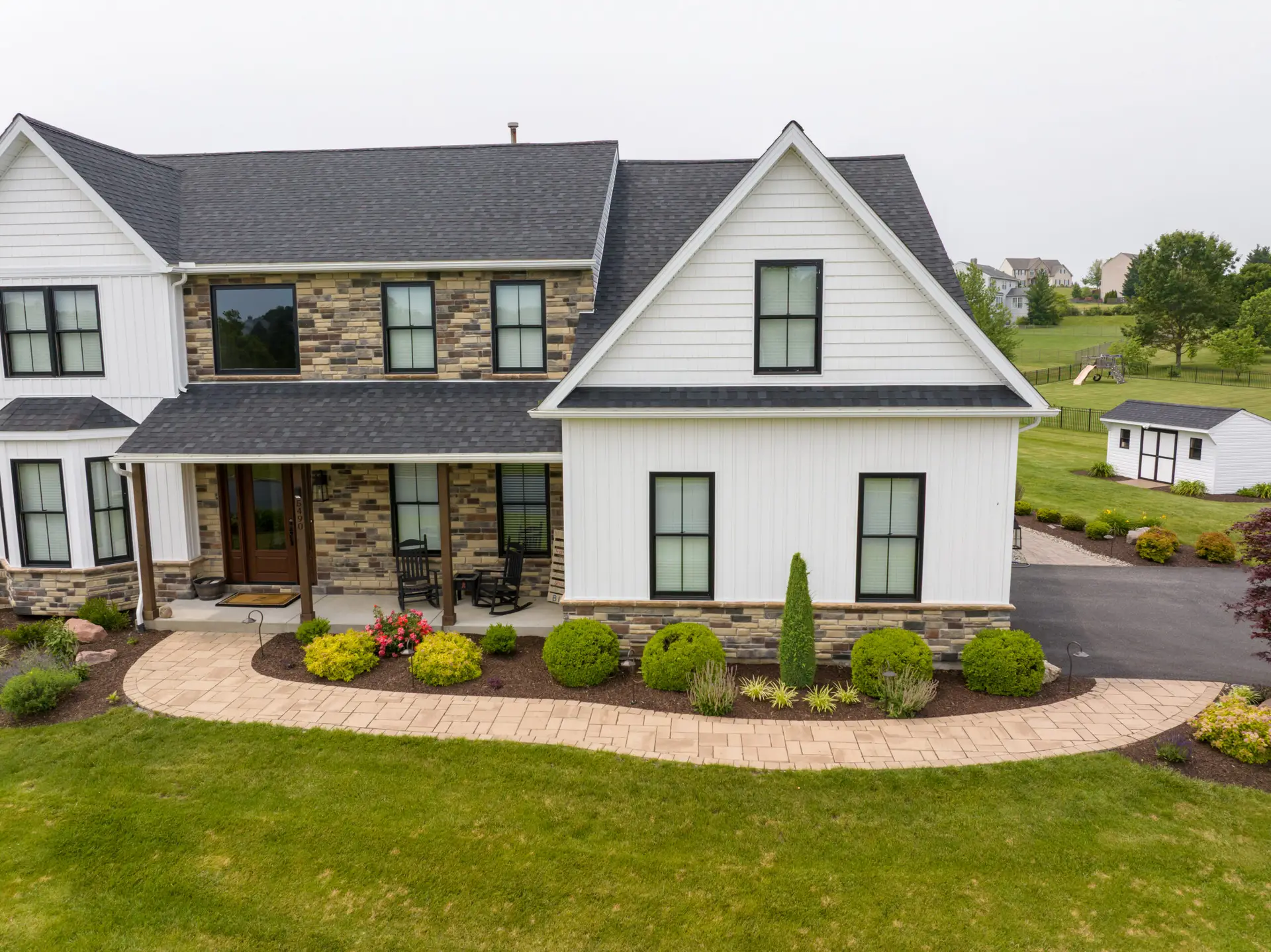 Front view of a modern two-story house with brick and white siding, a curved stone walkway, and manicured front yard.