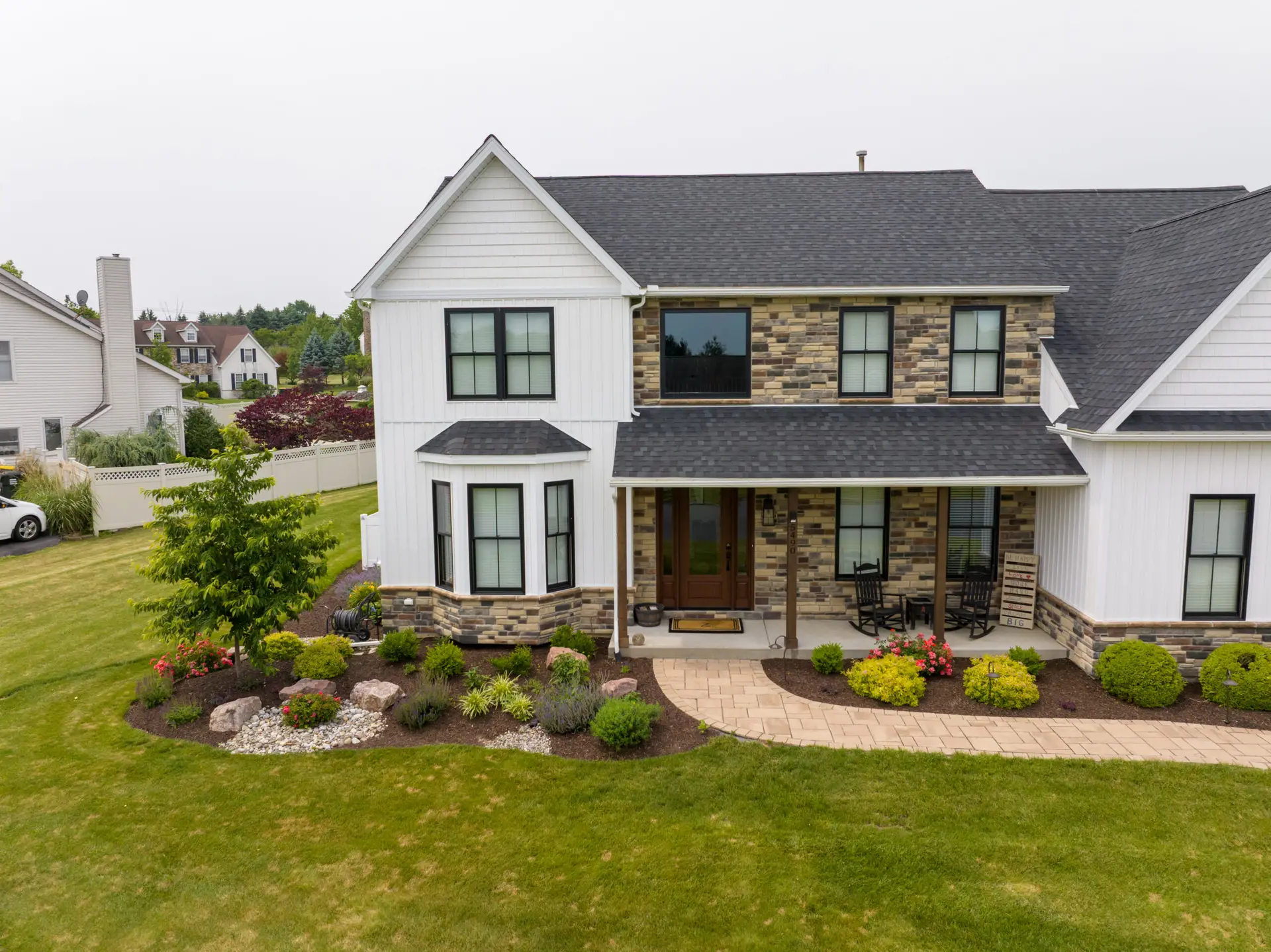 Two-story white house with stone accents, dark roof, and a curved brick path in the front yard.
