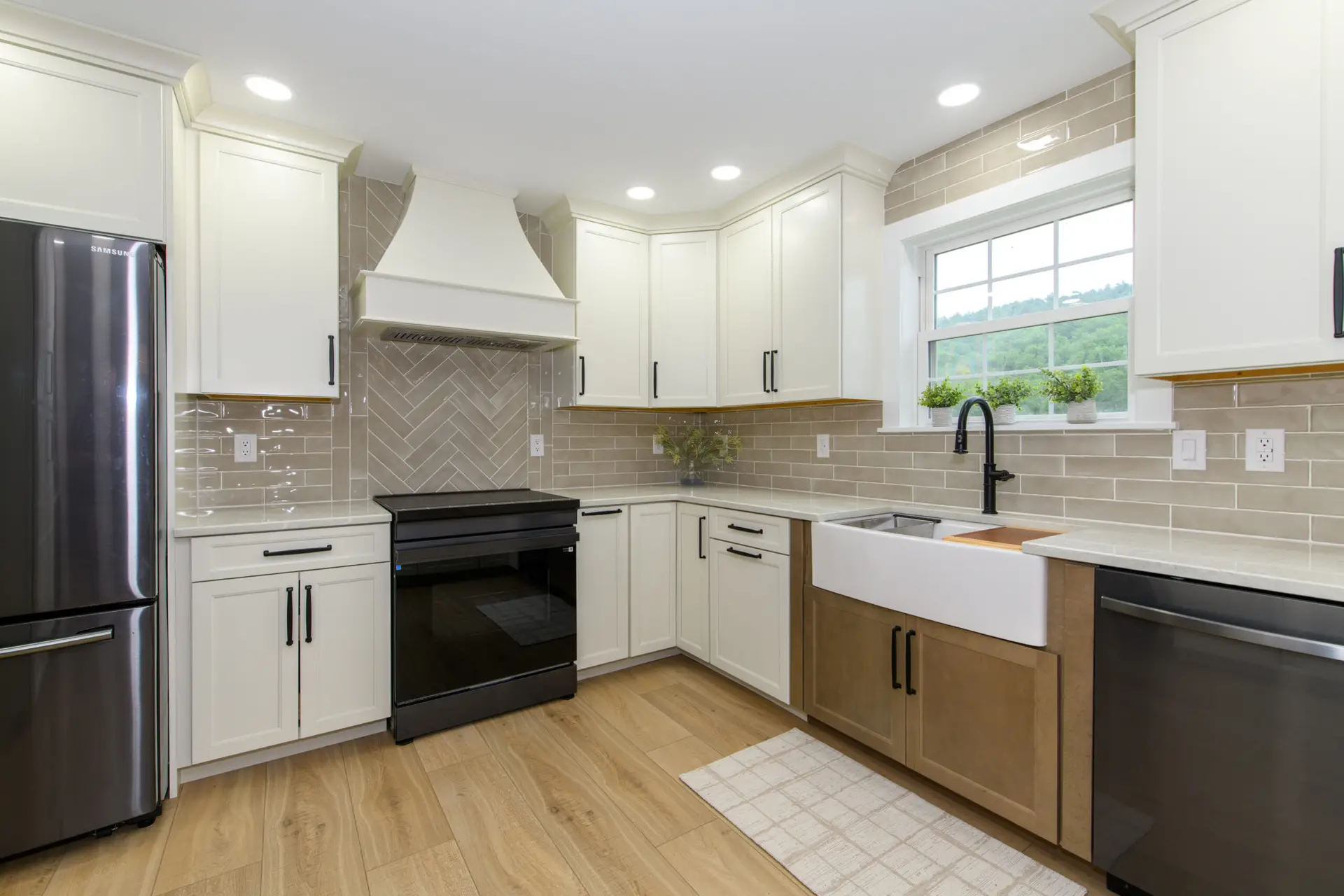 Bright modern kitchen with white cabinetry, stainless steel refrigerator, and black hardware; beige tile backsplash and large window.