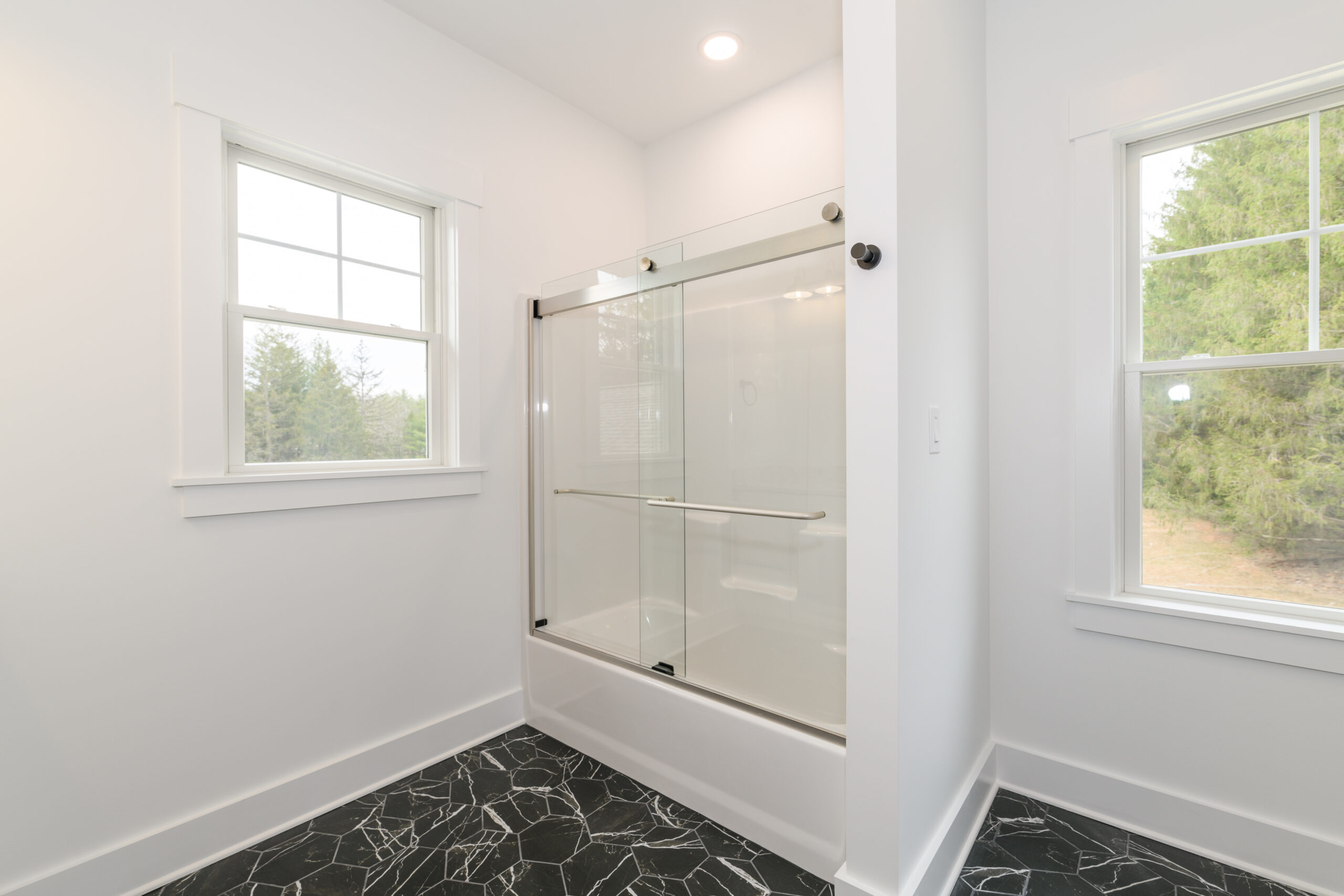 Bright bathroom with a glass shower enclosure, white walls, and black marble floor tiles at the base of the shower.