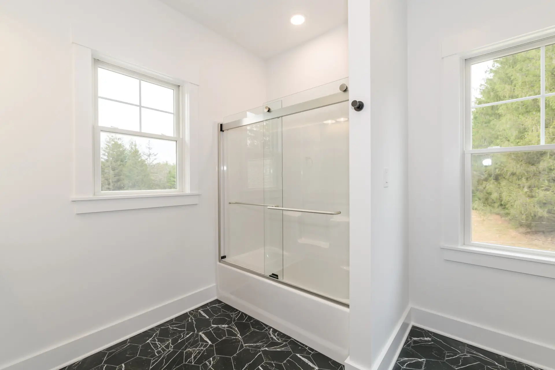 Bright bathroom with a glass shower enclosure, white walls, and black marble floor tiles at the base of the shower.