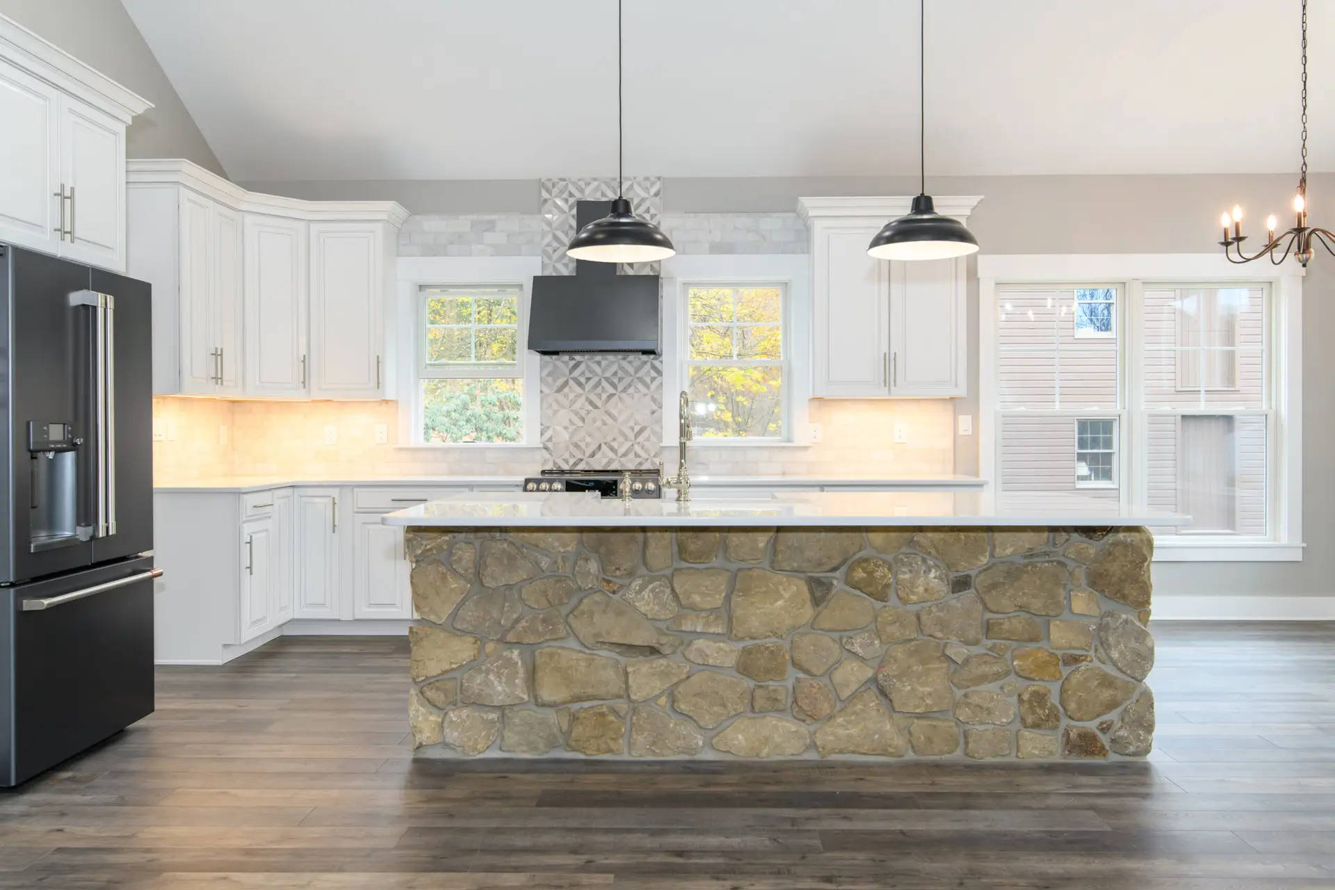 Modern kitchen featuring a stone-faced island, white cabinets, stainless steel fridge, and pendant lights above the counter.