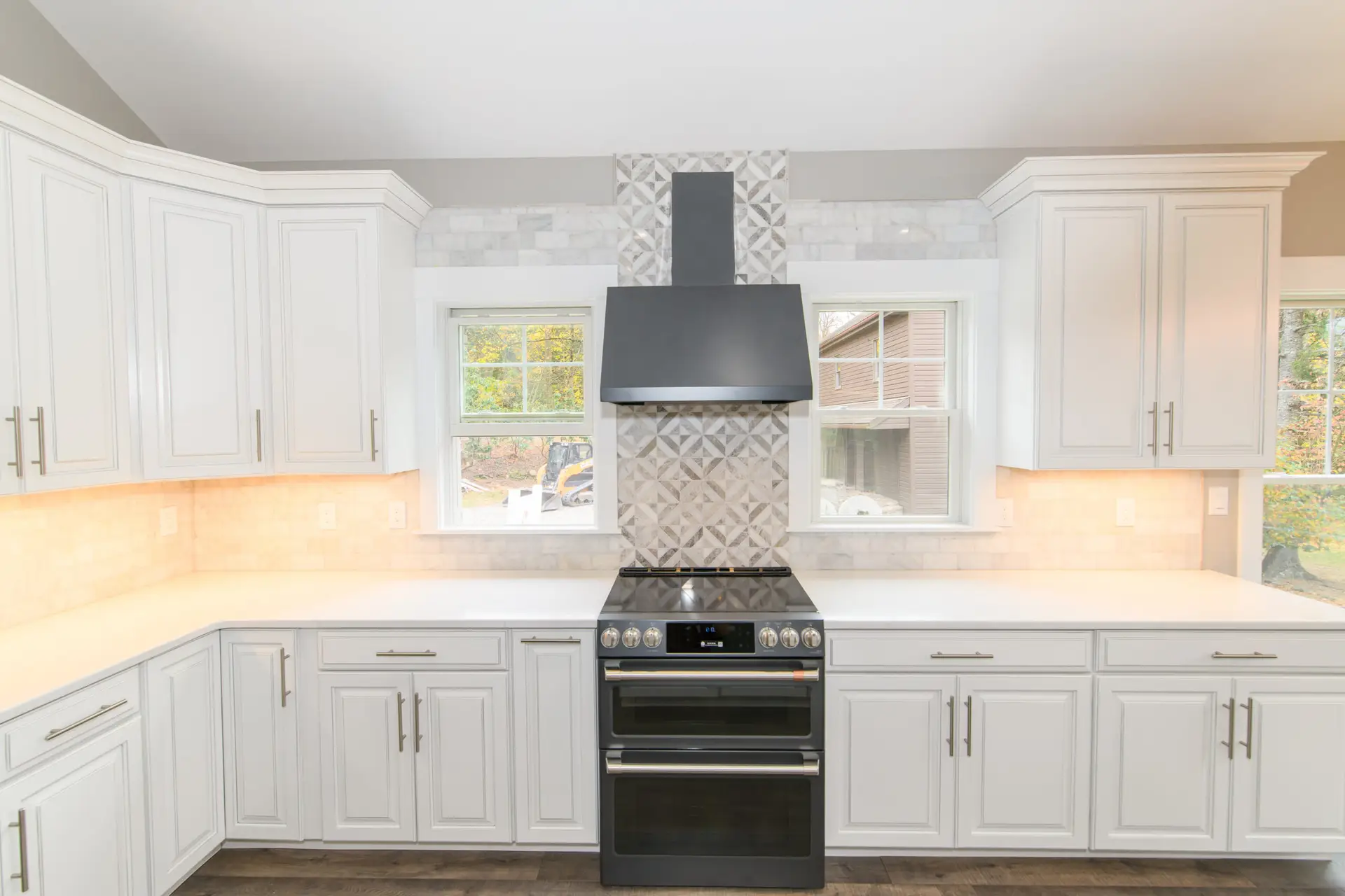 Modern white kitchen with white raised-panel cabinets, marble backsplash, and a black stainless range hood centered between two windows.