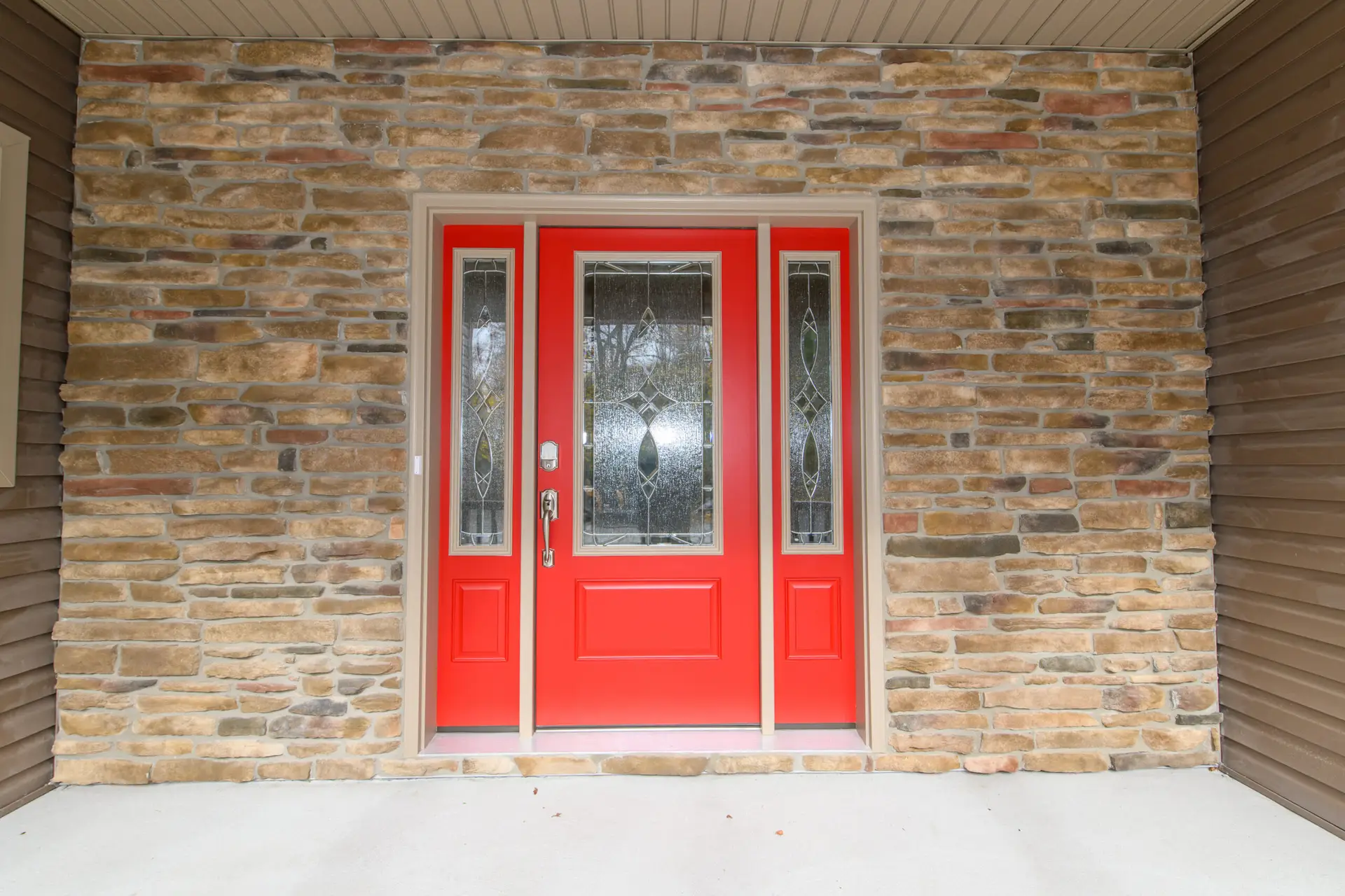 Front entry door: bright red with decorative glass panels set in a stone-clad entryway.