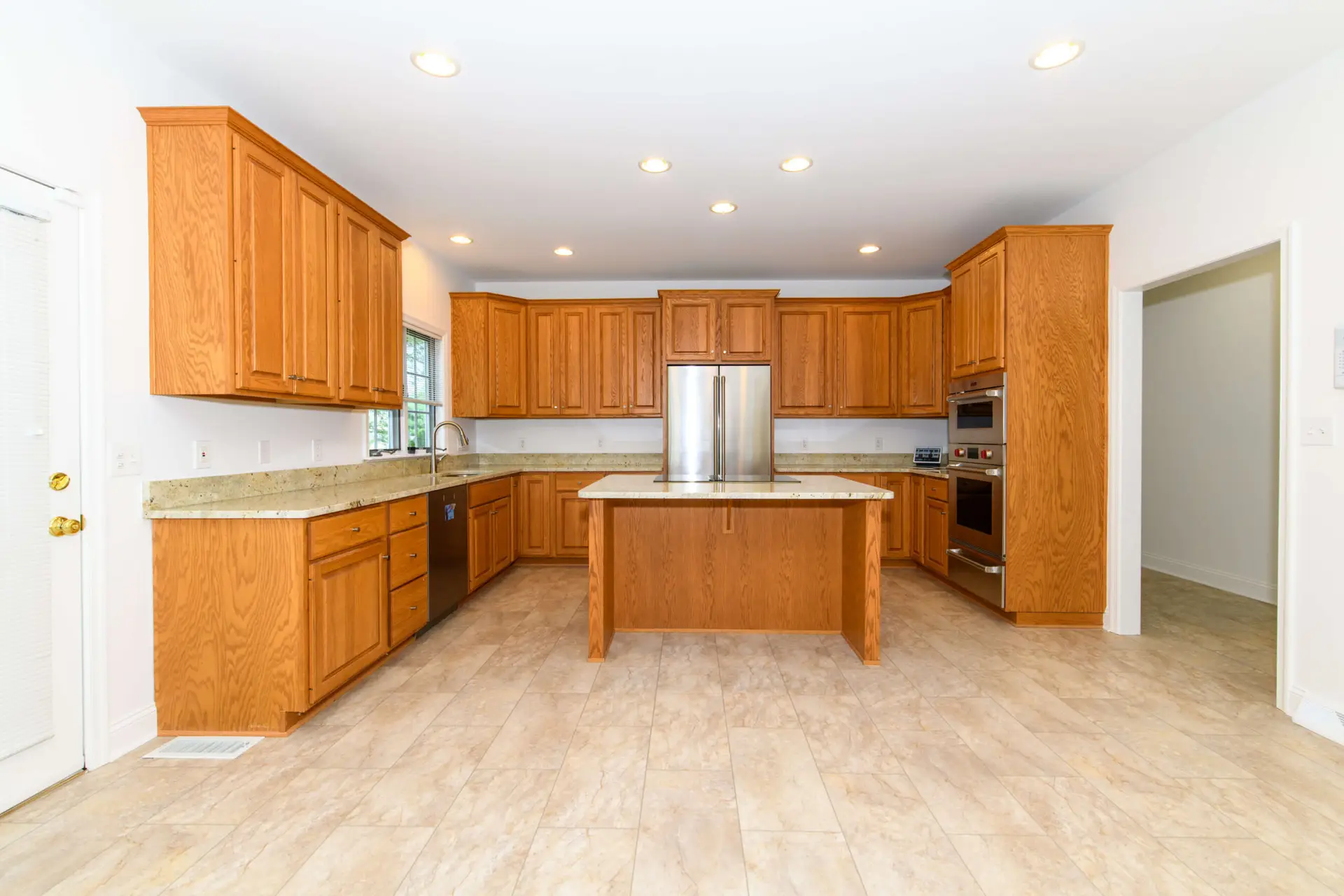 Bright kitchen with cherry wood cabinets, beige countertops, island in center, and stainless steel refrigerator and ovens.
