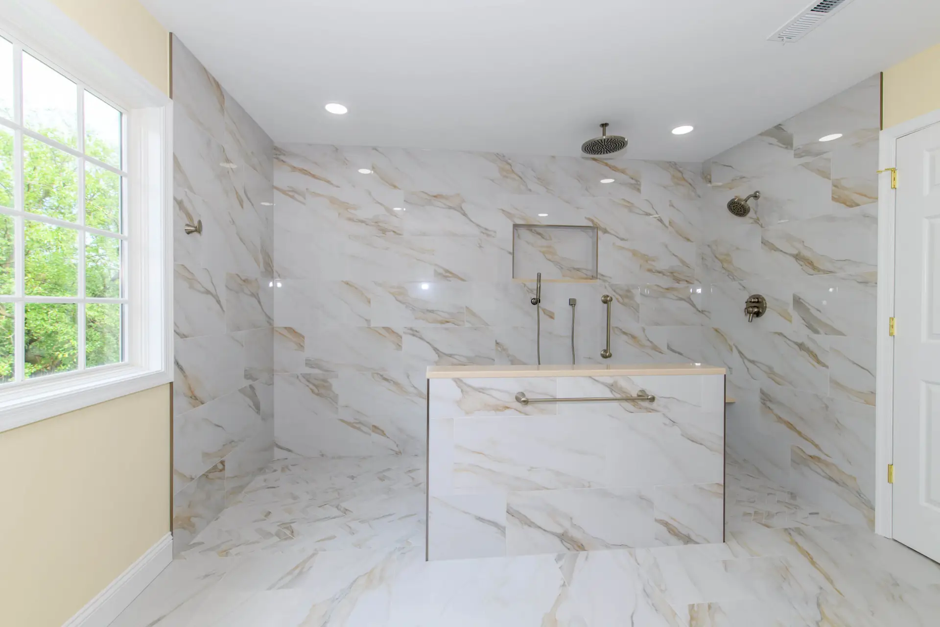 Bright marble-tiled bathroom with a large window, walk-in shower, ceiling rain shower, and multiple wall fixtures.