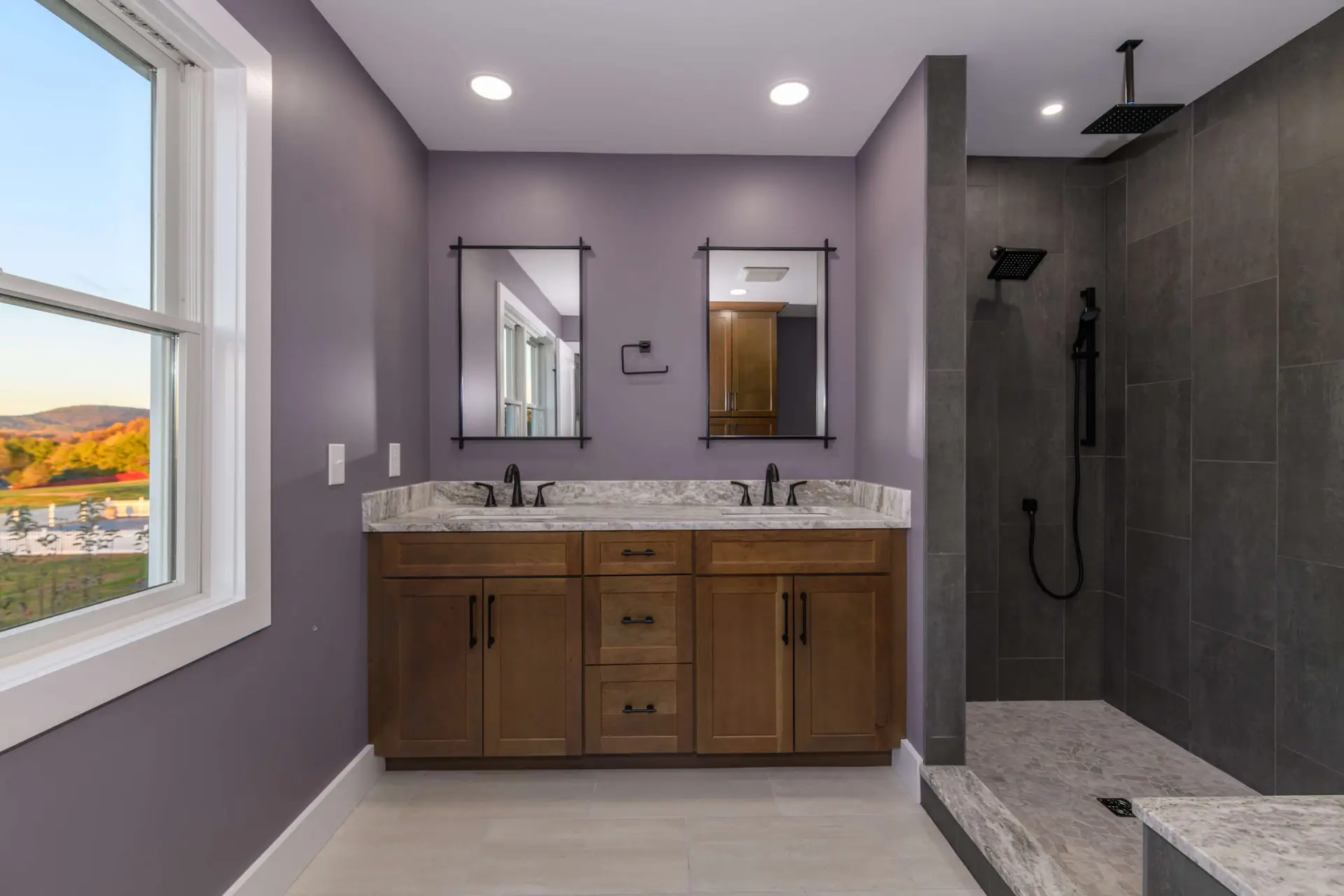 Modern bathroom with purple walls, wooden vanity, and granite countertop with two sinks and black fixtures.