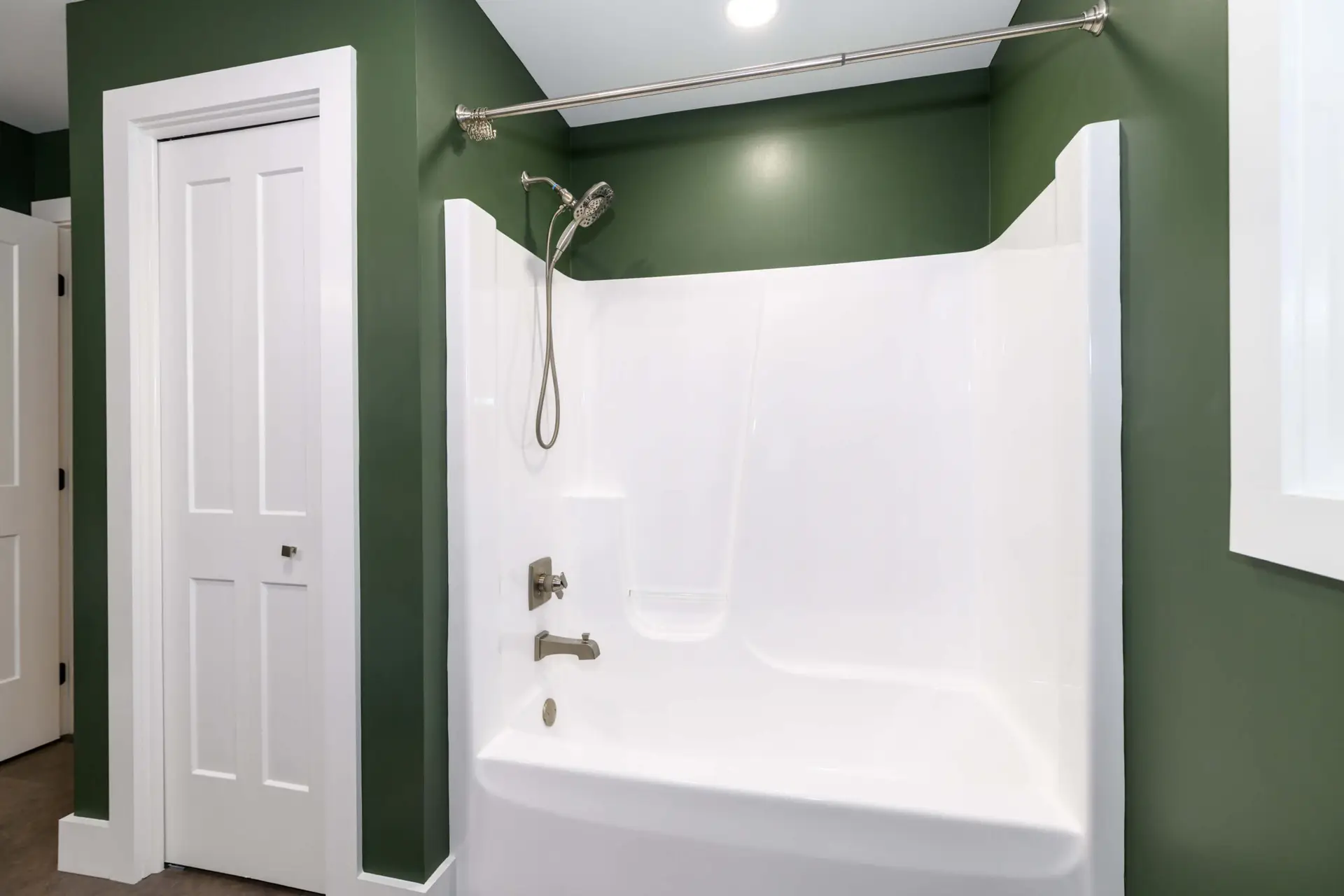 White built-in bathtub with handheld shower, green walls, and chrome fixtures.
