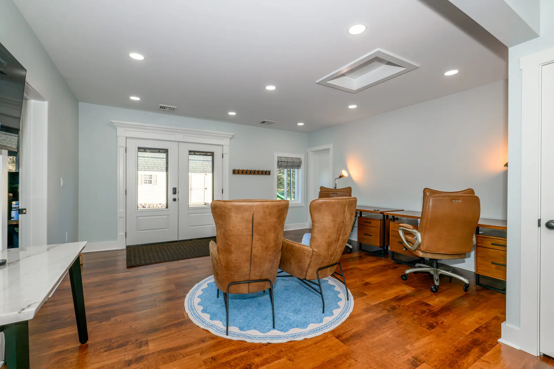 Office lounge with brown leather chairs around a blue circular rug near white double doors and wood floors.