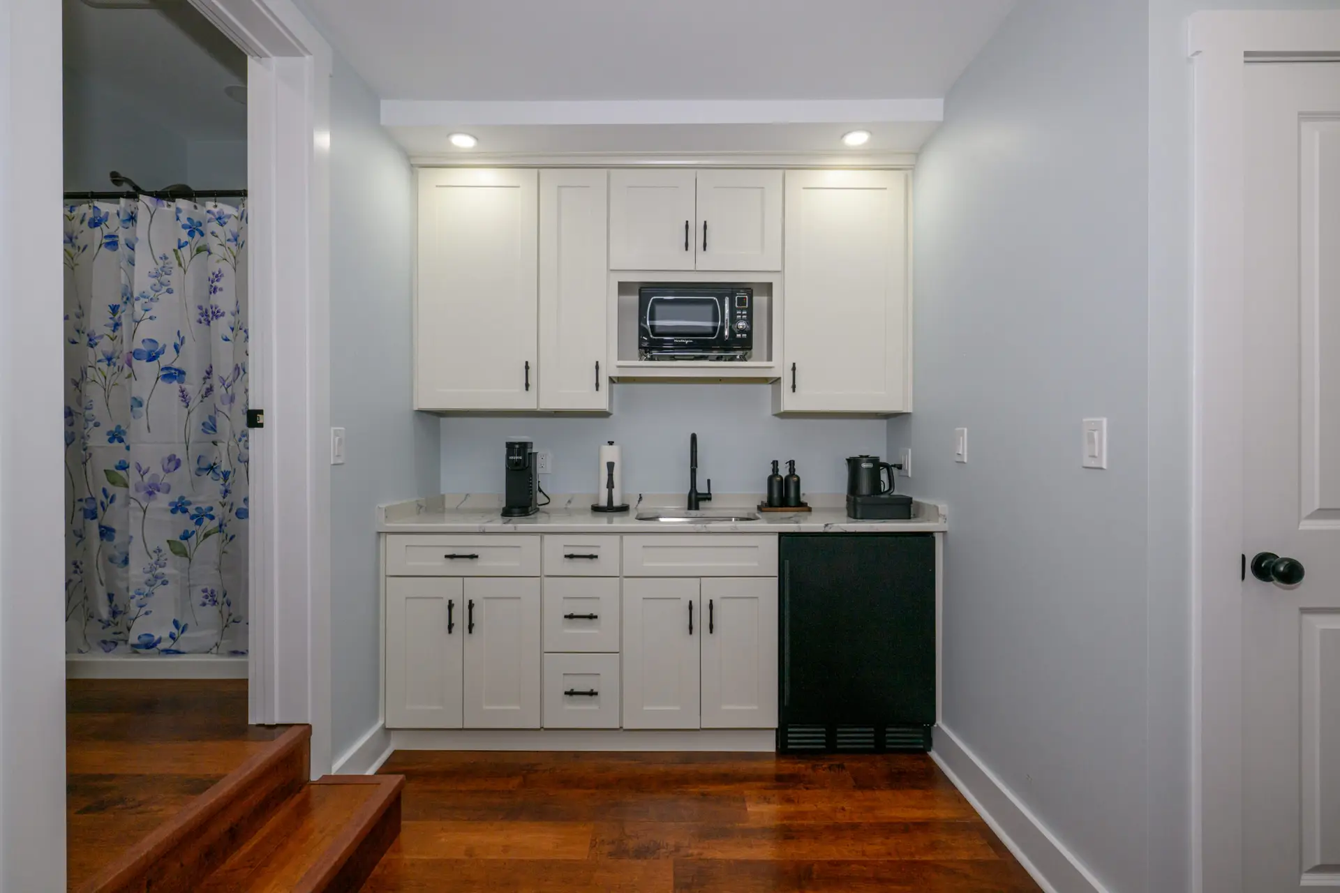 Modern white kitchen with upper cabinets, built-in microwave, and dark small appliances on a marble countertop.