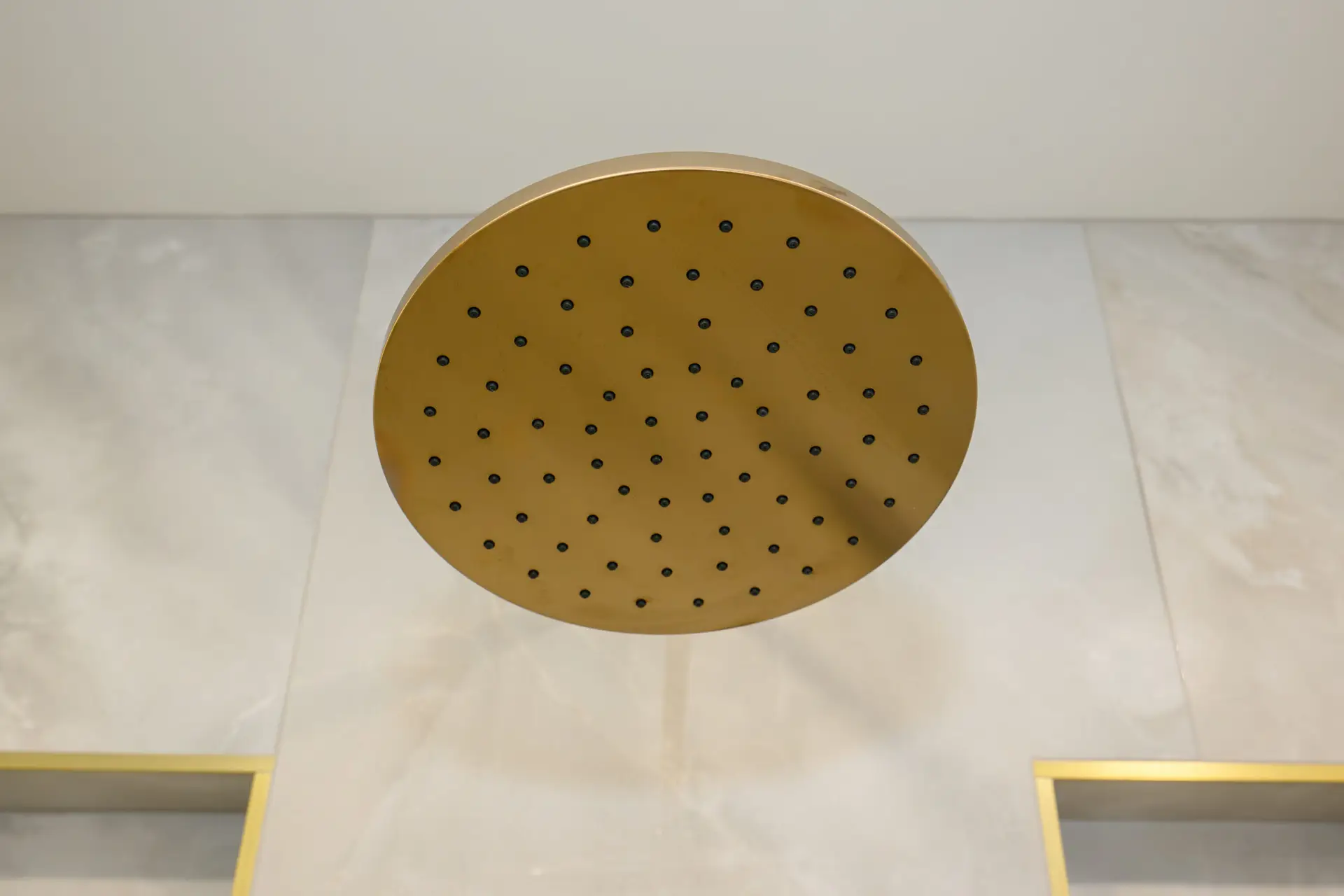 Large gold circular shower head viewed from below against a light tiled ceiling.