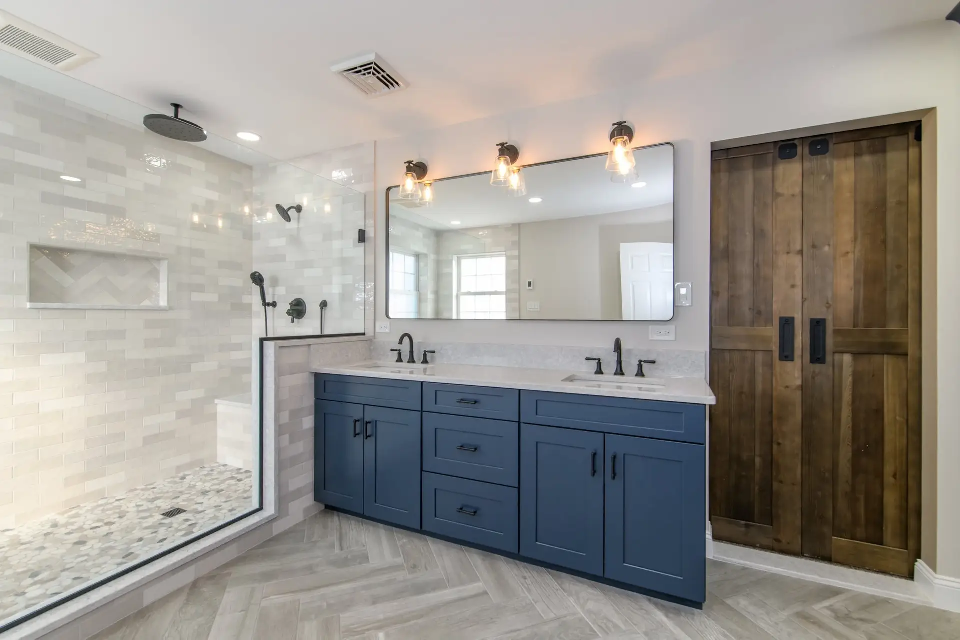 Bathroom Remodel Cost - TNY Contracting - TNY Contracting Modern bathroom with blue cabinets, large mirror, and double sinks; glass-enclosed shower and textured tile walls are on the left.