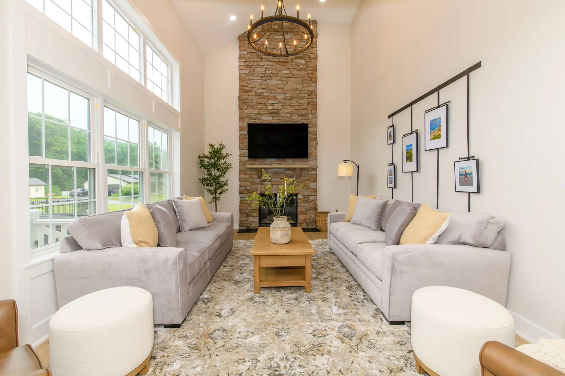 Bright living room with a tall stone fireplace, a wall-mounted TV, and two gray sofas facing a wooden coffee table.”