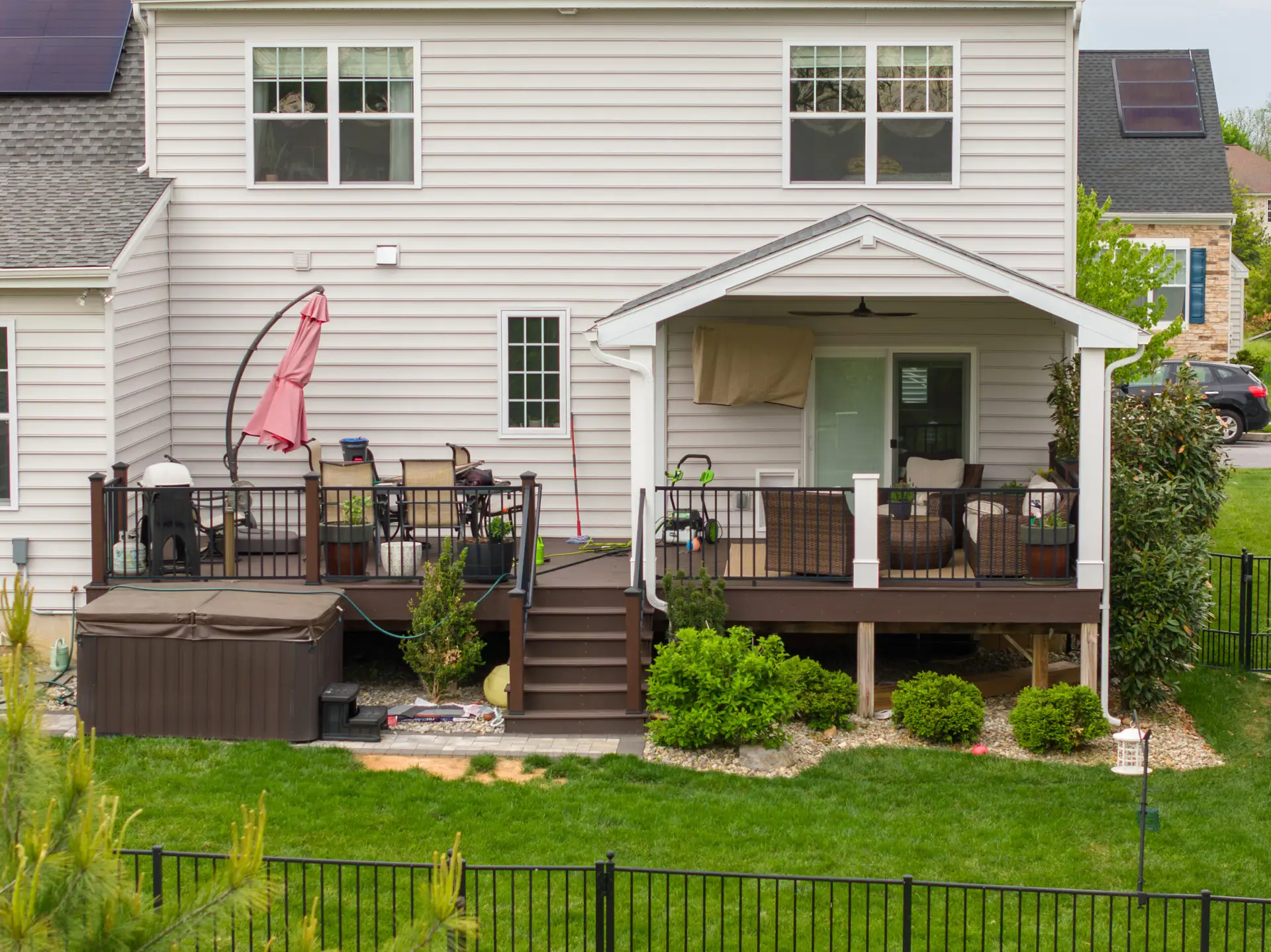 Backyard patio of a beige two-story house with a covered seating area, outdoor furniture, and a pink umbrella on the deck.
