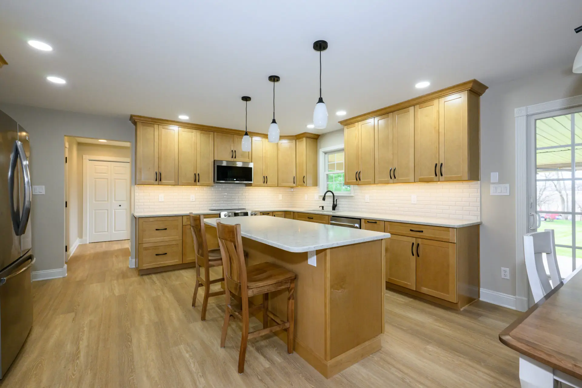 Bright kitchen with natural wood cabinets, white countertops, and three pendant lights over the island.