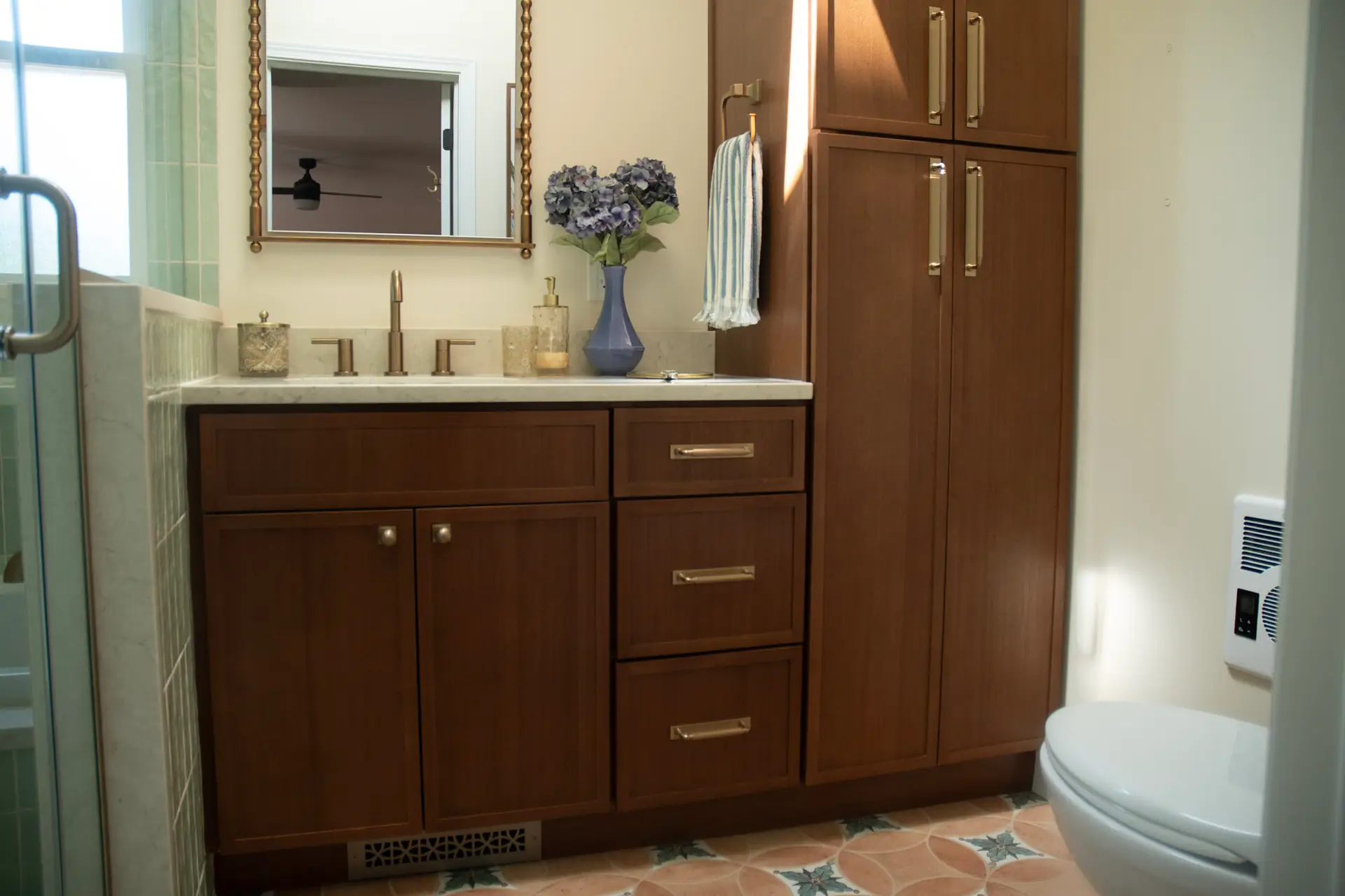 Bathroom vanity with dark wood cabinets, marble countertop, bronze faucet, and a blue vase of purple hydrangeas on the counter.