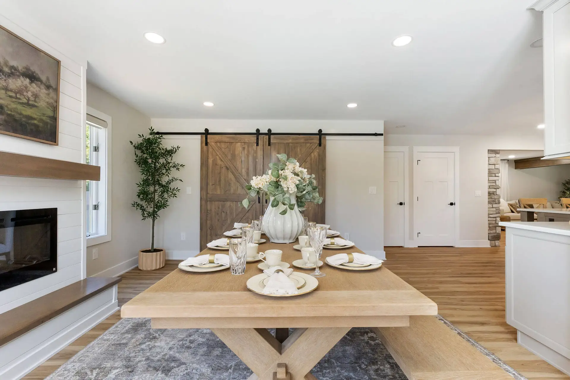 Dining room table set for a meal with white dishes, glassware, and a large floral centerpiece in a bright, modern farmhouse space